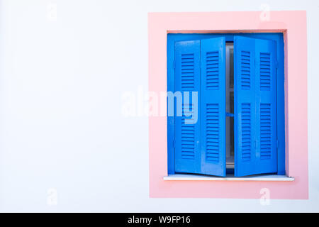 Eine Studie der blauen Fensterläden auf einem Rosa Fenster auf einem weißen Haus in Fiskardo, Kefalonia, Griechenland. Stockfoto