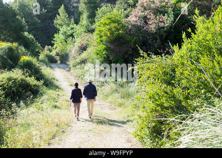 Eine abenteuerliche Paar in gehen früh ihre späten 60er 70er auf einen Weg mit Wildblumen und Sträucher in Kefalonia Griechenland gesäumt. Stockfoto