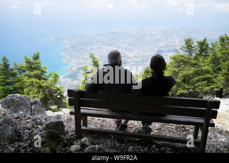 Ein Mann und eine Frau sitzen auf einer Bank mit Blick auf die Insel Kefalonia und das Ionische Meer von der Spitze des Berges Ainos. Stockfoto