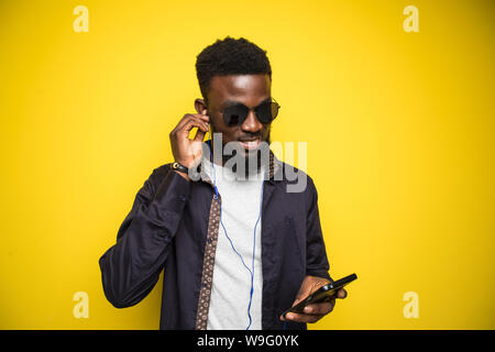 Junge afrikanische Mann in Sonnenbrille tragen Kopfhörer und Musik tanzen über Gelb Hintergrund Stockfoto