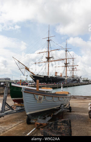 HMS Warrior angedockt in Portsmouth mit zwei alte hölzerne Boote im Vordergrund. Stockfoto