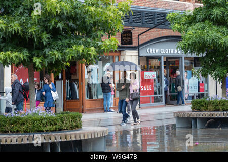 Ein paar nehmen Schutz vor dem Regen unter einem Sonnenschirm beim gehen Vergangenheit Schaufenster in einem Einkaufszentrum Stockfoto