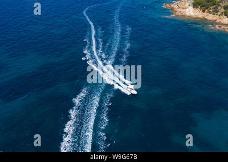 Ansicht von oben, atemberaubenden Blick auf einem kleinen Boot segeln auf einem wunderschönen türkisen Meer, taucht die Grünen und felsigen Küsten Sardiniens. Stockfoto