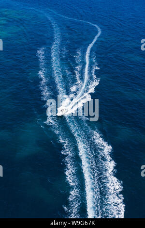 Ansicht von oben, atemberaubenden Blick auf einem kleinen Boot segeln auf einem wunderschönen türkisen Meer, taucht die Grünen und felsigen Küsten Sardiniens. Stockfoto