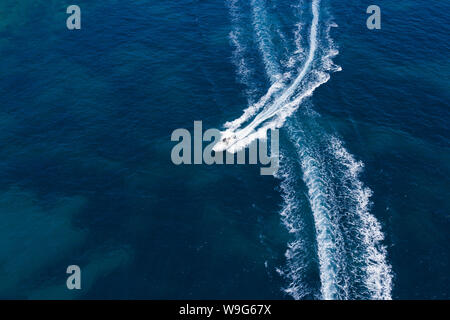 Ansicht von oben, atemberaubenden Blick auf einem kleinen Boot segeln auf einem wunderschönen türkisen Meer, taucht die Grünen und felsigen Küsten Sardiniens. Stockfoto