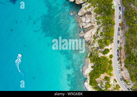 Ansicht von oben, atemberaubenden Blick auf eine Straße, die entlang der felsigen Küste von einem Türkis und transparenten Meer gebadet. Cala Gonone, Sardinien, Italien. Stockfoto