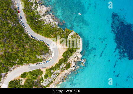 Ansicht von oben, atemberaubenden Blick auf eine Straße, die entlang der felsigen Küste von einem Türkis und transparenten Meer gebadet. Cala Gonone, Sardinien, Italien. Stockfoto