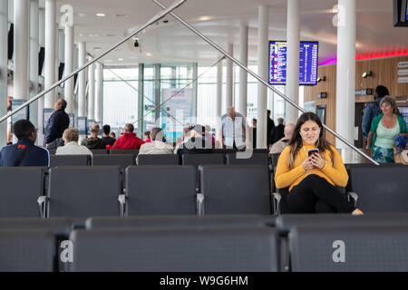 Eine junge Frau, die an Ihrem Telefon mit Kopfhörern in lächelnd im Sitzen warten, ein Terminal für den Transport zu gelangen Stockfoto