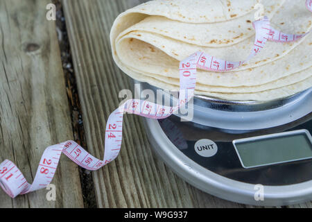 Low carb Tortillas auf einer Skala mit Maßband auf Holz- Hintergrund. Leeren leeren Raum für Text oder kopieren. Gesund Gesundheit essen Trend für ke Stockfoto