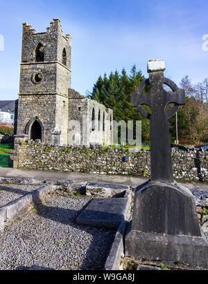 Grabstein in der Form eines keltischen Kreuz mit der Heiligen Maria des Rosenkranzes Katholische Kirche im Hintergrund in der Nähe von Cong, County Mayo, Irland Stockfoto