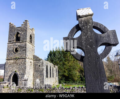 Grabstein in der Form eines keltischen Kreuz mit der Heiligen Maria des Rosenkranzes Katholische Kirche im Hintergrund in der Nähe von Cong, County Mayo, Irland Stockfoto