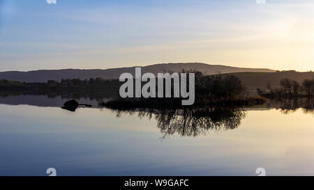 In den stillen Wassern des Lough Corrib, County Galway, Irland ist die Reflexion über die umliegenden Berge und Inseln bei Sonnenuntergang Stockfoto