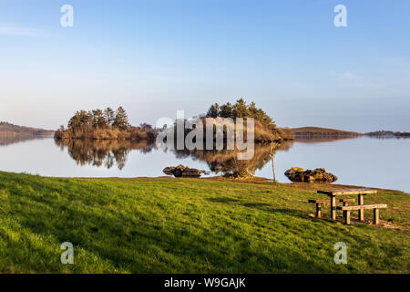 In den stillen Wassern des Lough Corrib, County Galway, Irland ist die Reflexion über die umliegenden Berge und Inseln bei Sonnenuntergang Stockfoto