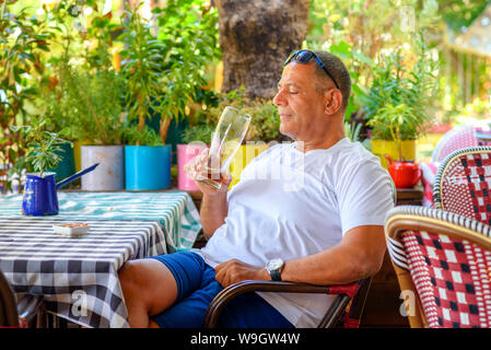 Im Nahen und Mittleren Osten man Bier trinkt. Seitenansicht des gutaussehenden Mann mittleren Alters trinken Bier, während Sitzen im Restaurant im Freien Terrasse. Stockfoto