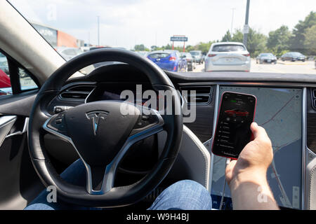 Mann mit Tesla mobile App auf dem iPhone beim Parken, Aufladen bei Tesla Kompressor. Stockfoto