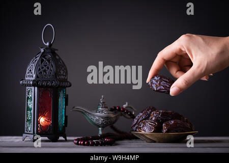 Ramadan Essen und Getränke Konzept. Frau Hand reicht, um eine Platte mit Datum mit Ramadan Laterne mit arabischen Lampe, Holz Rosenkranz, Tee, Obst und Termine Stockfoto