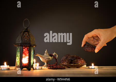 Ramadan Essen und Getränke Konzept. Frau Hand reicht, um eine Platte mit Datum mit Ramadan Laterne mit arabischen Lampe, Holz Rosenkranz, Tee, Obst und Termine Stockfoto