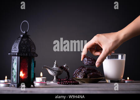 Ramadan Essen und Getränke Konzept. Frau Hand reicht, um eine Platte mit Datum mit Ramadan Laterne mit arabischen Lampe, Holz Rosenkranz, Tee, Obst und Termine Stockfoto