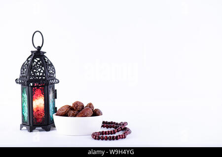 Ramadan Essen und Getränke Konzept. Ramadan Laterne mit arabischen Lampe, Holz Rosenkranz, Kaffee, Obst und Beleuchtung an einem Holztisch auf weißem Hintergrund. Stockfoto