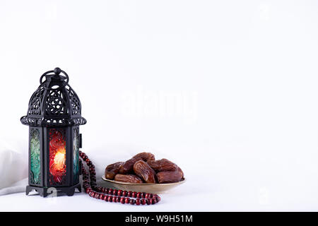 Ramadan Essen und Getränke Konzept. Ramadan Laterne mit arabischen Lampe, Holz Rosenkranz, Kaffee, Obst und Beleuchtung an einem Holztisch auf weißem Hintergrund. Stockfoto