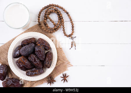 Ramadan Essen und Getränke Konzept. Holz Rosenkranz, Milch und Obst auf einem weißen Tisch Hintergrund. Ansicht von oben, flach. Stockfoto