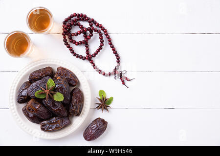 Ramadan Essen und Getränke Konzept. Holz Rosenkranz, Tee und Datteln Obst auf einem weißen Tisch Hintergrund. Ansicht von oben, flach. Stockfoto