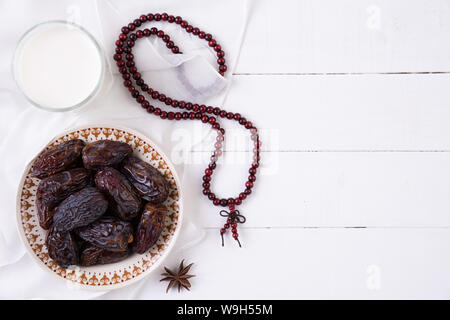 Ramadan Essen und Getränke Konzept. Holz Rosenkranz, Milch und Obst auf einem weißen Tisch Hintergrund. Ansicht von oben, flach. Stockfoto