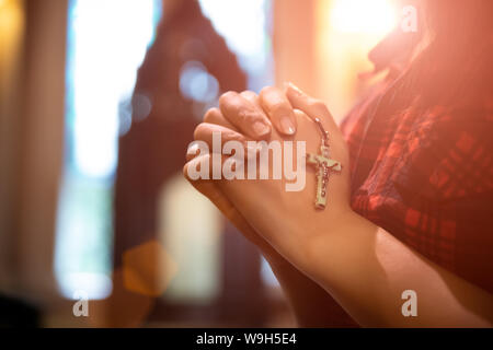 Frau hand Rosenkranz gegen Kreuz und beten zu Gott in der Kirche. Stockfoto