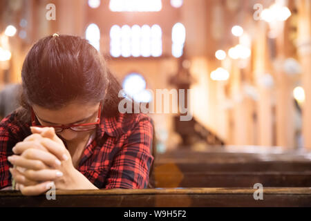 Junge Frau sitzt auf einer Bank in der Kirche und betet zu Gott. Hände gefaltet im Gebet Konzept für den Glauben. Stockfoto