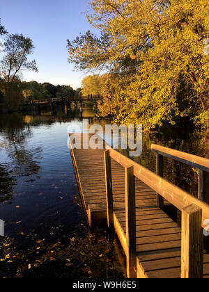 Herbst Blick auf ein Dock, die sich über das Wasser mit der Old North Bridge in der Ferne und im Wasser widerspiegelt. Concord, MA. Stockfoto