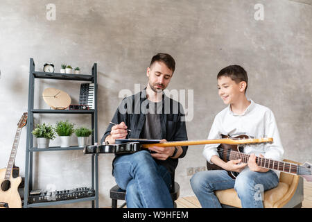 Wenig student Uhren zu seiner Musik, Lehrer, Noten auf Musik Blatt schreibt. Stockfoto