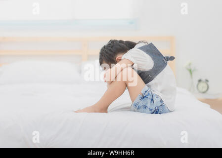 Deprimiert asiatische Mädchen sitzen auf dem Bett auf die Knie und umarmte in traurige Moody. Foto Design für Familie und Kind Konzept. Stockfoto