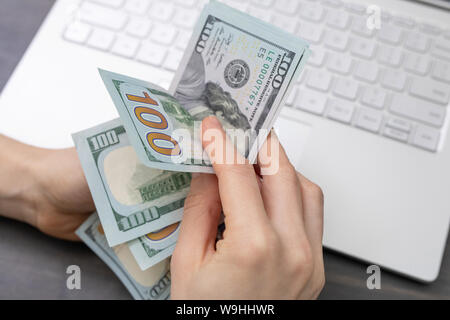 Der Mensch zählt Geld, Dollar in der Hand. Laptop auf Hintergrund Stockfoto