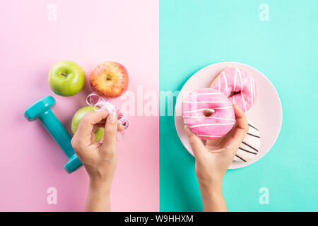 Gesunde Lebensweise, Ernährung und Sport Konzept. Blick von oben auf die Frau hand Donut und Maßband mit Ausrüstung des Athleten Hantel, grün rot Apple Stockfoto