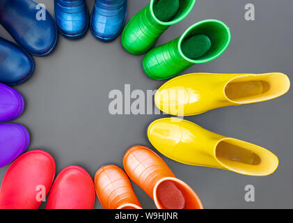 Bunte Gummistiefel in allen Farben des Regenbogens - Rot, Orange, Gelb, Grün, Blau, Türkis und Violett stehen auf der grauen Fläche im Kreis. Ansicht von oben, Stockfoto