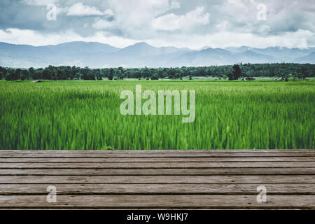 Grünes Feld mit hölzernen Tischplatte Vordergrund leeren Platz für Werbung. Reis Bereich im freien Blick auf das Meer. Stockfoto