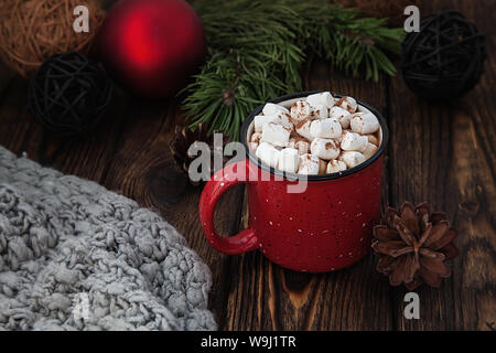 Eine rote Tasse mit heißem Getränk mit Marshmallow und Strickschal auf Holz Weihnachten Hintergrund Stockfoto