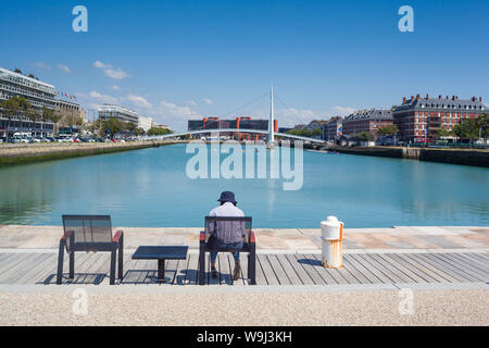 Ein Mann in einem Hut sitzt Lesung im Sonnenschein am Bassin du Commerce, Le Havre, Normandie Stockfoto