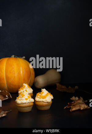 Kürbis Cupcakes auf einem dunklen Hintergrund, Herbst Hintergrund verschiedene Kürbisse und Blätter. Kürbis Süßigkeiten. Halloween und Thanksgiving Süßigkeiten. Vertikale Stockfoto