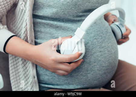 Schwangere Frau Kopfhörer setzen auf ihrem Abdomen Stockfoto