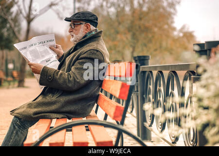 Seitliche Sicht auf ein älterer Mann lesen Zeitung in Park Stockfoto