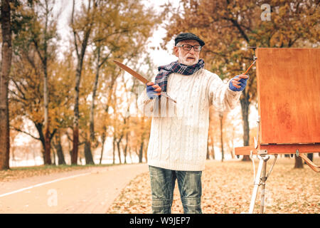 Gut aussehender älterer Mann Malerei im herbstlichen Park Stockfoto