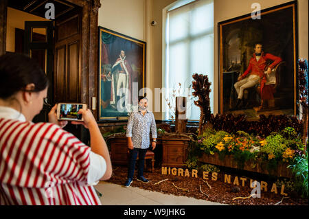 Brüssel, Brabant, Belgien. 14 Aug, 2019. Eine Frau nimmt ein Foto von einem Der mexikanische Künstler mit seinen floralen Kunst während der Anlass. Blüte Zeit ist eine zweijährige Initiative, die 2013 von der Stadt Brüssel und die ASBL (gemeinnützige Organisation) Tapis de Fleurs de Bruxelles" ins Leben gerufen wurde. Unter dem Motto "Eine Welt der floralen Emotionen", mehr als 30 top Floristen aus 13 Ländern die herrlichen Zimmer von Brussels City Hall, die von der Unesco zum Meisterwerk gotischer Architektur eingerichtet. Brüssel' berühmten Grand Place veranstaltet zu diesem Anlass einen atemberaubenden Blume arch aus 500 Fuchsien. Dieser y Stockfoto