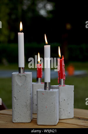 Rote und weiße Kerzen brennen auf einen Tisch im Freien. Kerzenhalter sind aus Beton und Stahl. Stockfoto