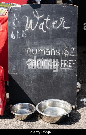 Schiefertafel Zeichen an einem Bauern markt mit Wasser mit Menschen die Preise': $ 2 Eckzähne: KOSTENLOS" mit 2 Metall hund Becher voll Wasser Stockfoto