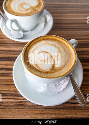 Zwei Tasse Cappuccino und Latte Kunst auf Holz- Hintergrund. Heißer Kaffee auf Tisch. Von der Seite. Schönen Schaum Stockfoto