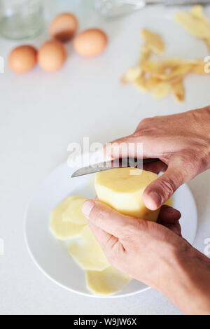 Nahaufnahme von einem kaukasischen Mann in der Küche schneiden einige Kartoffeln, zu einem typischen Tortilla de patatas bereiten, ein spanisches Omelette Stockfoto