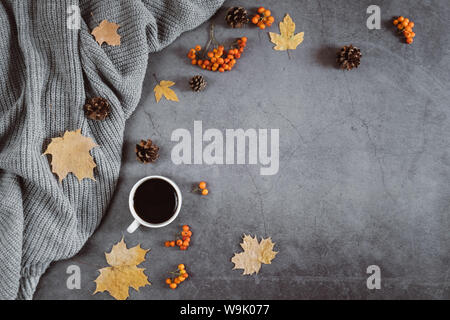 Winter Zusammensetzung. Eine Tasse Kaffee, Pullover, Kegel, berry Rowan und Blätter im Herbst Ahorn auf dunklen konkreten Hintergrund. Herbst, Winter Konzept. Flach Stockfoto