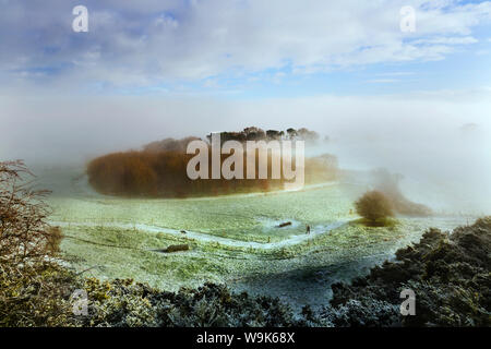 Eine Dame zu ihrem Hund über einen Fußweg unten Eddisbury Hill auf einem eisigen Wintern morgen mit Nebel und Dunst Clearing über, Cheshire, England, Großbritannien Stockfoto