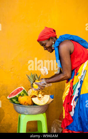 Frau gekleidet in traditionelle Kleidung schneiden und Verkauf von Obst in die farbenfrohe Altstadt von Cartagena, Kolumbien, Südamerika Stockfoto